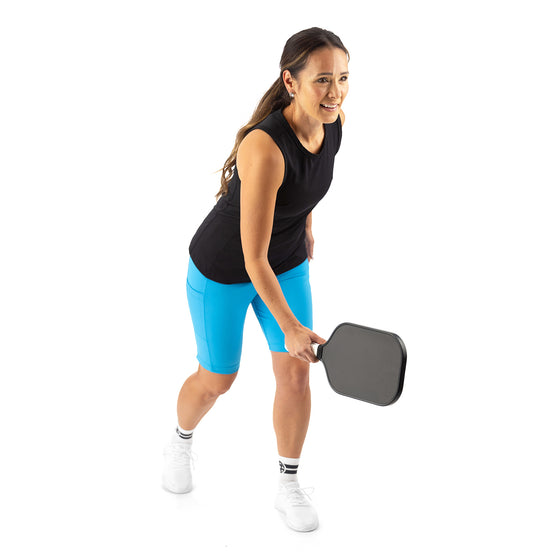 Woman wearing Saltie Rose Pickleball Outfit—black racerback top and electric blue 9" shorts.