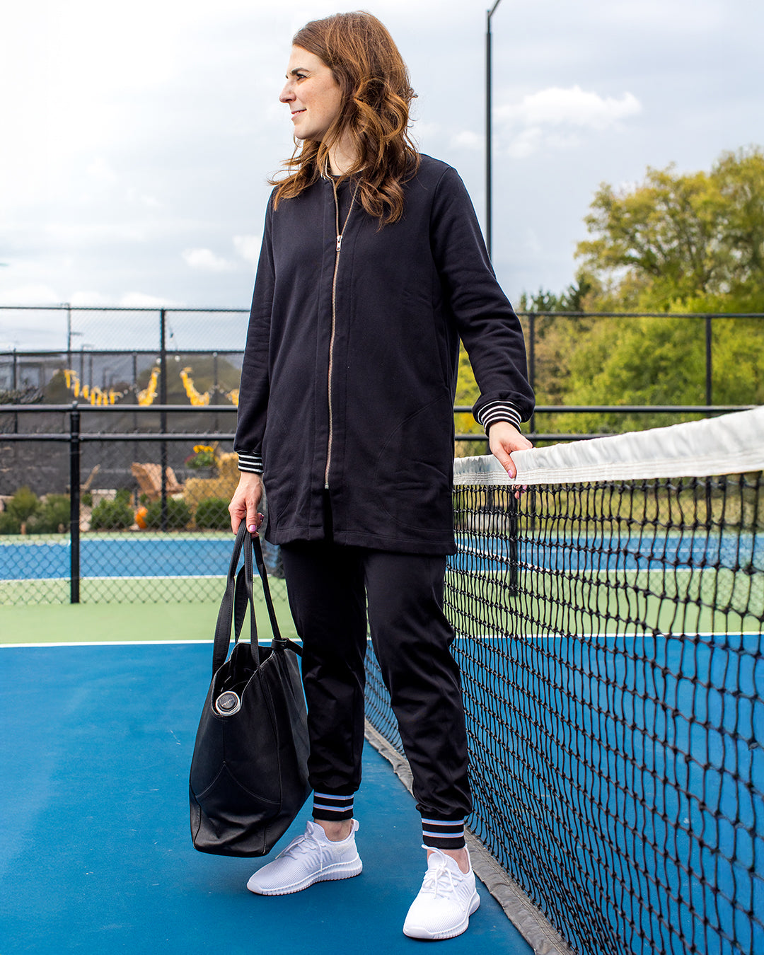 Woman wearing saltie rose pickleball black long bomber  jacket. 